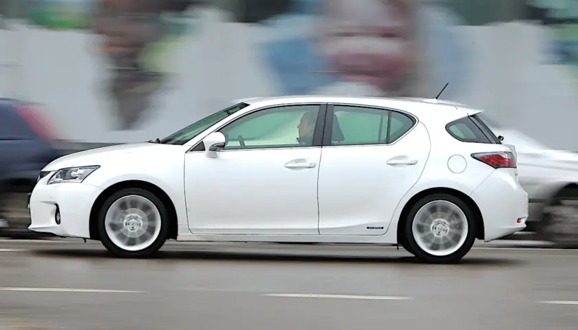 Biały Lexus CT200h w ruchu ulicznym, z rozmytym tłem i innymi samochodami.