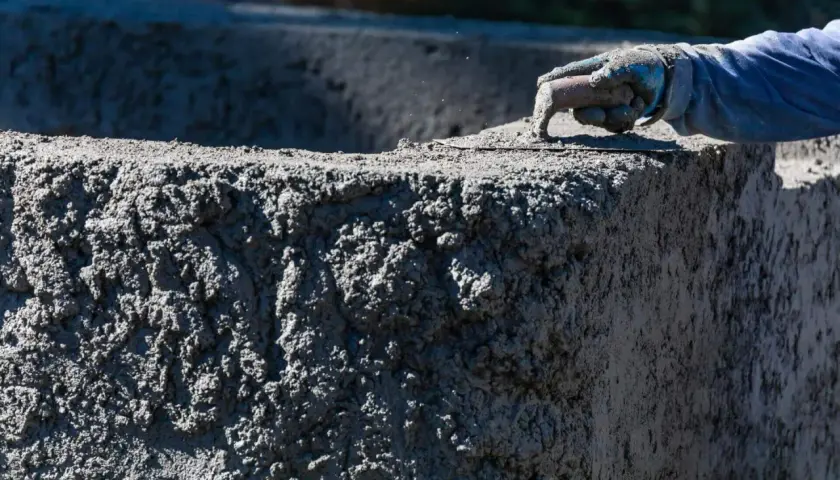 Ręka w rękawicy wygładza świeży beton. Zastanawiasz się, ile kosztuje worek cementu do takiej pracy?