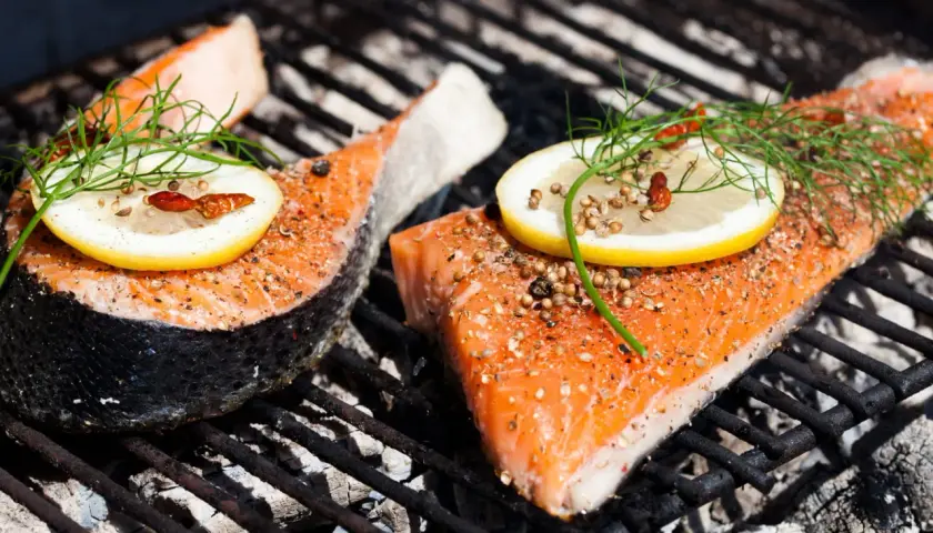 Deux pavés de saumon au barbecue, assaisonnés et garnis de citron et d'aneth, cuisent sur une grille chaude.