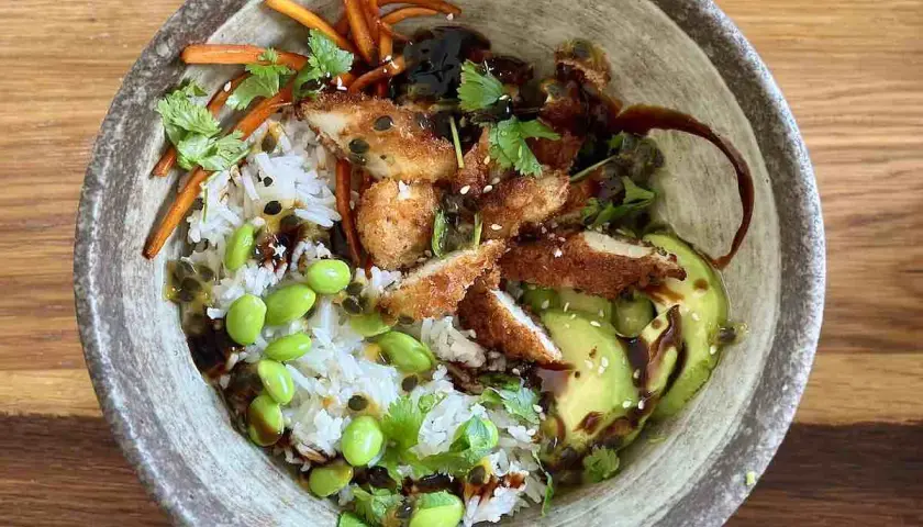 Apetyczny bowl z kurczakiem w panierce, ryżem, awokado, edamame i słodko-kwaśnym sosem.