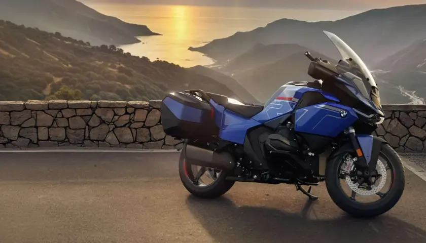 Una moto blu pronta per un viaggio avventuroso, parcheggiata su una strada panoramica con montagne e mare al tramonto.