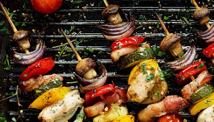 Brochettes de poulet et de legume bbq sur un grill, avec des poivrons, courgettes, oignons rouges, champignons et tomates.