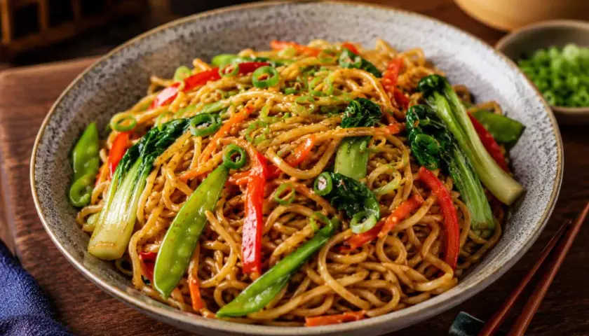 Pyszny makaron chow mein z warzywami, posypany sezamem i szczypiorkiem. Idealny na szybki obiad.