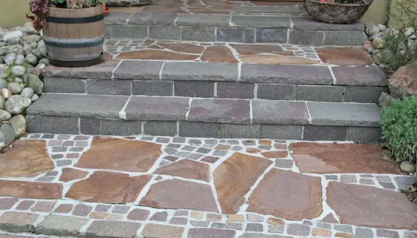 Stufen mit polygonalplatten verlegen. Große, unregelmäßige Steinplatten wechseln sich mit kleinen, quadratischen Pflastersteinen ab.