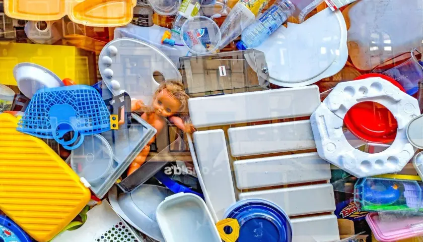 Kolorowy stos plastikowych odpadów, w tym butelki, pojemniki i zabawki. To przykład tego, co to są surowce wtórne.
