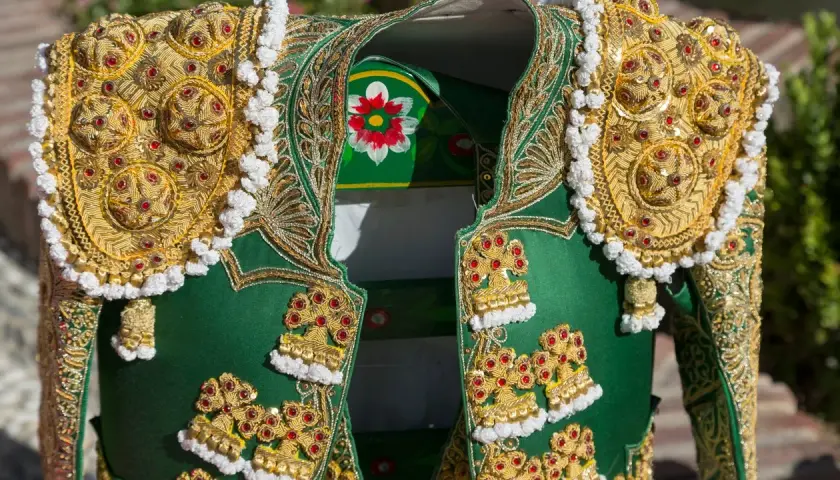 Detalle de un traje de luces de torero, con bordados dorados y pedrería roja sobre tela verde.