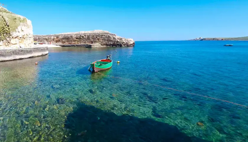 Un bateau vert et rouge flotte dans les eaux cristallines de Polignano a Mare, dans les Pouilles. Le soleil brille sur la mer Adriatique.