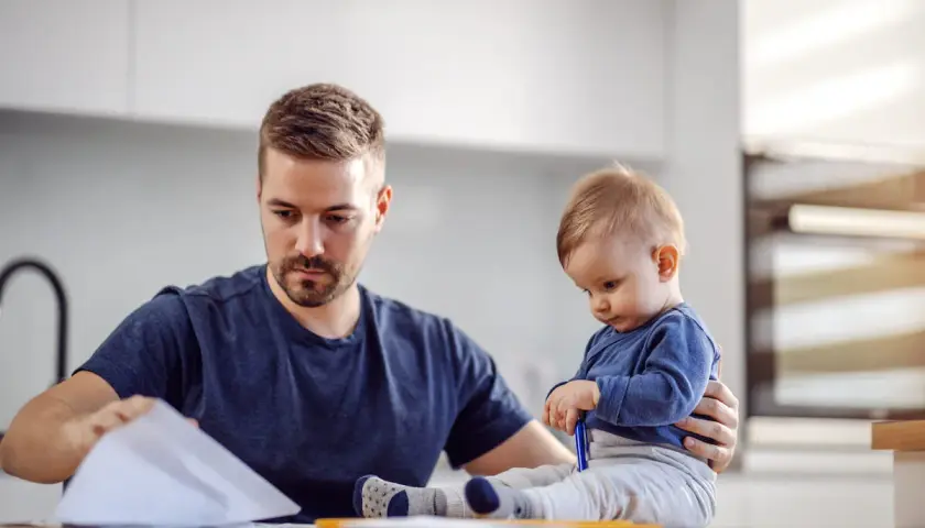 Ojciec pracuje w domu, a dziecko siedzi obok, bawiąc się długopisem. To obraz codziennych kontaktów z dzieckiem w miejscu zamieszkania matki.