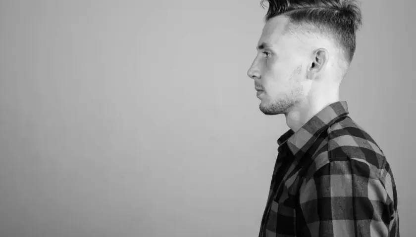 Perfil de hombre con un corte de pelo taper fade moderno y camisa a cuadros.