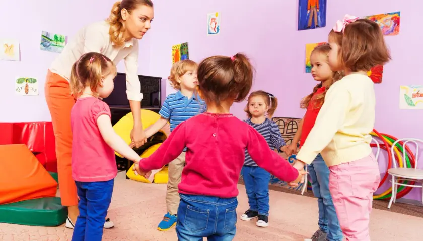 Nauczycielka z dziećmi w przedszkolu trzymają się za ręce. Czy można przenieść dziecko do innej grupy bez zgody rodziców?