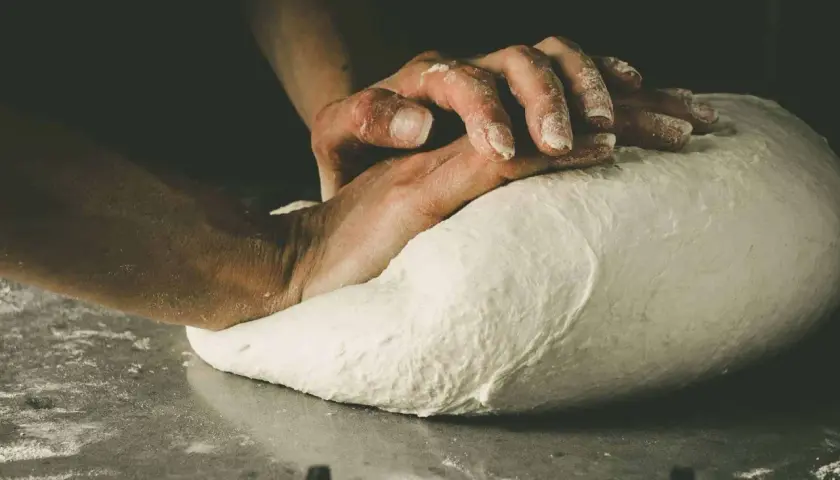 Hände kneten den Pizzateig. Die Frage "wie lange pizzateig kneten" beschäftigt jeden Bäcker.