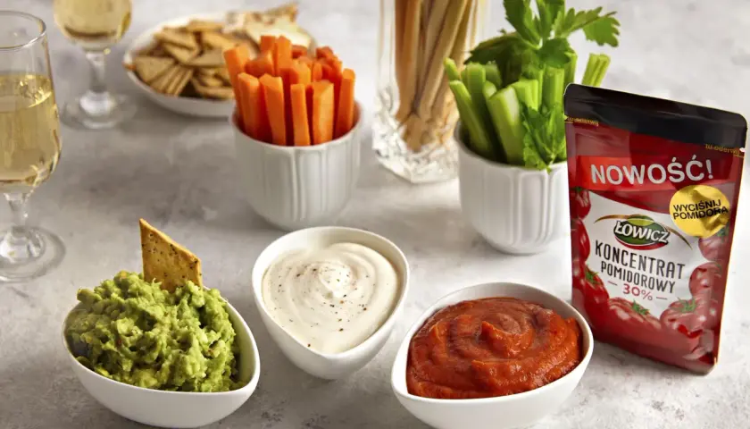 Trzy miseczki z dipami: guacamole, śmietanowym i pomidorowym, obok warzyw i krakersów.