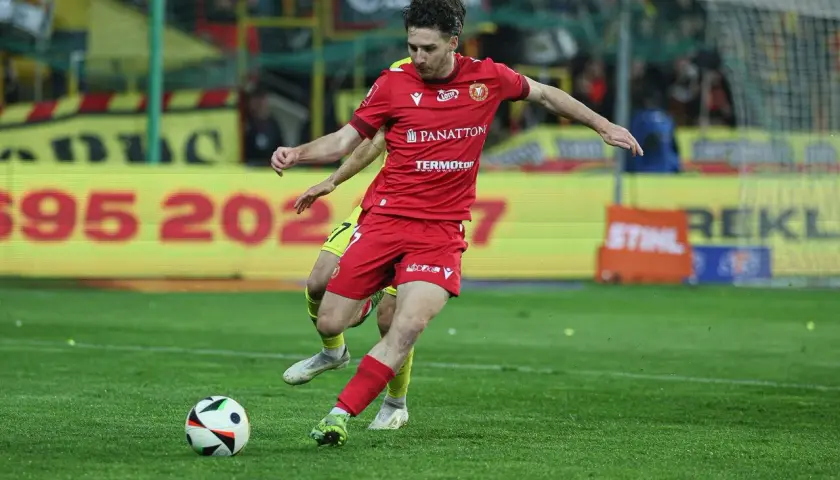 GKS Katowice piłkarze w akcji. Zawodnik w czerwonej koszulce drybluje z piłką na boisku, walcząc o zwycięstwo.