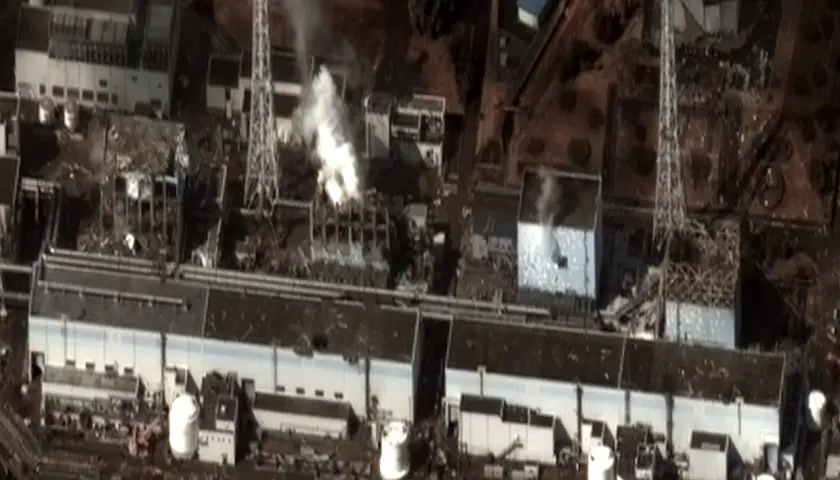 Widok z lotu ptaka na zniszczoną elektrownię Fukushima. Widać dym wydobywający się z uszkodzonych budynków, świadectwo katastrofy.