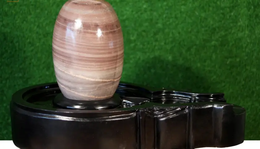 En vackert randig shiva linga av sten vilar på ett svart, glänsande altare.