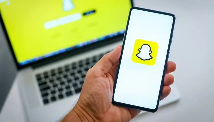 Chcesz wiedzieć, jak usunąć konto na Snapie? Na ekranie telefonu widać logo Snapchata, a na laptopie ekran logowania.