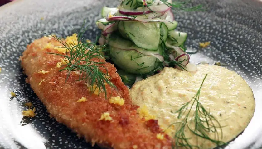 Panerad fisk med en krämig remouladsås curry, garnerad med dill och citronskal. Serveras med en fräsch gurk- och rödlökssallad.