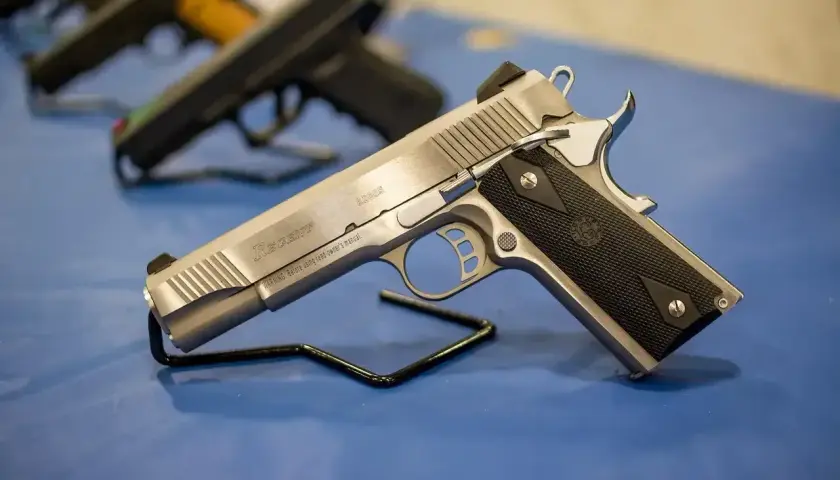 Srebrny pistolet gazowy Regent R200S na czarnym stojaku. W tle widać inne bronie.