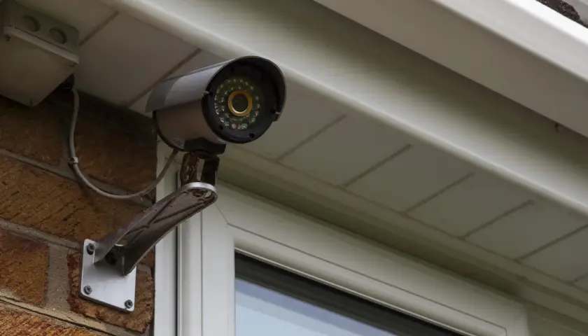 Telecamera di sicurezza, parte di un impianto di videosorveglianza, montata su una parete di mattoni sotto una grondaia.