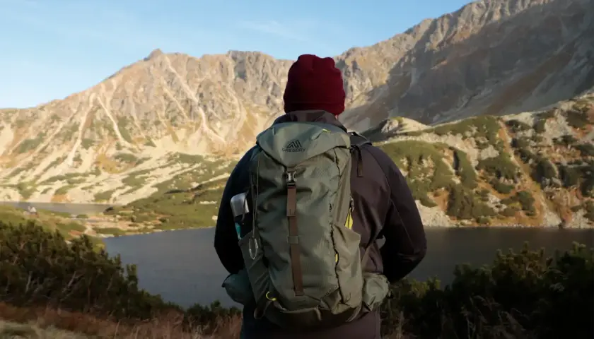 Turysta z plecakiem Gregory Jade 33 podziwia jesienny krajobraz górski z jeziorem.