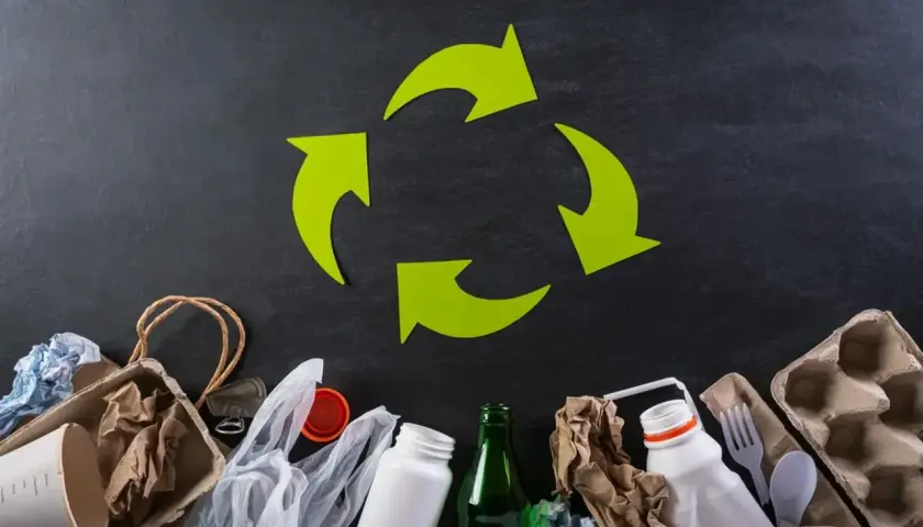 Zielony symbol recyklingu nad różnymi odpadami: papier, plastik, szkło.