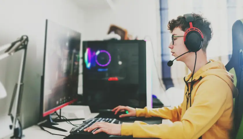 Ein junger Mann mit Kopfhörern und Brille spielt konzentriert am Computer. Sein **Computer sucht** nach neuen Herausforderungen, während er mit Tastatur und Maus agiert.