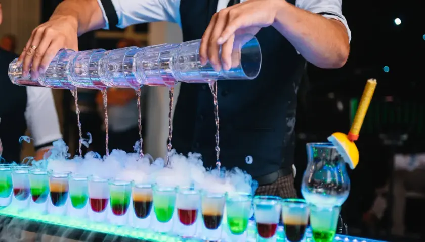 Samoobsługowy drink bar na weselu: barman nalewa kolorowe shoty z wielokomorowego shakera, tworząc efektowny pokaz.