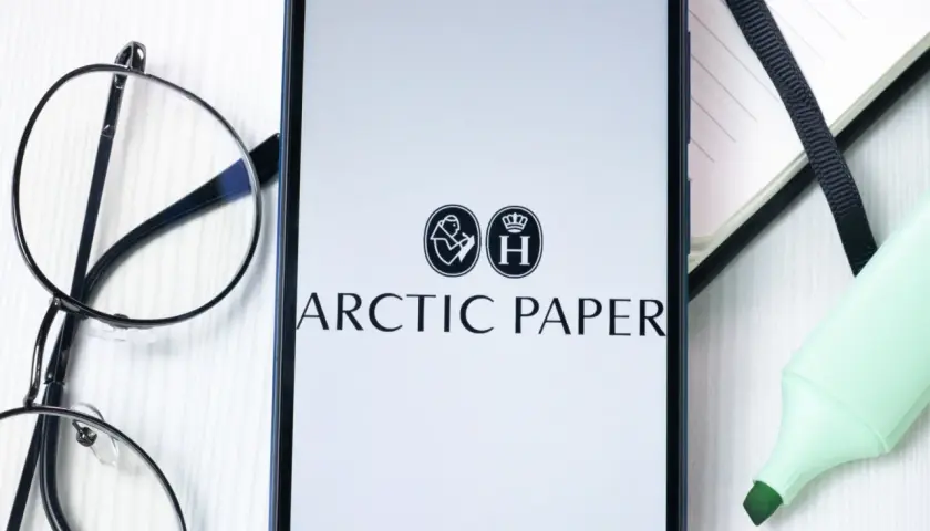 Na ekranie telefonu widnieje logo Arctic Paper. Obok leżą okulary i zielony zakreślacz, sugerując analizę akcji.