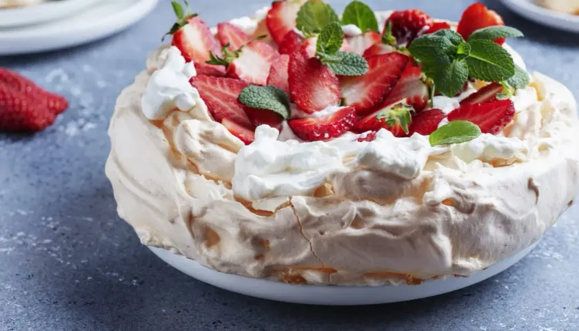 Puszysty tort bezowy z mascarpone i bitą śmietaną, ozdobiony świeżymi truskawkami i miętą.