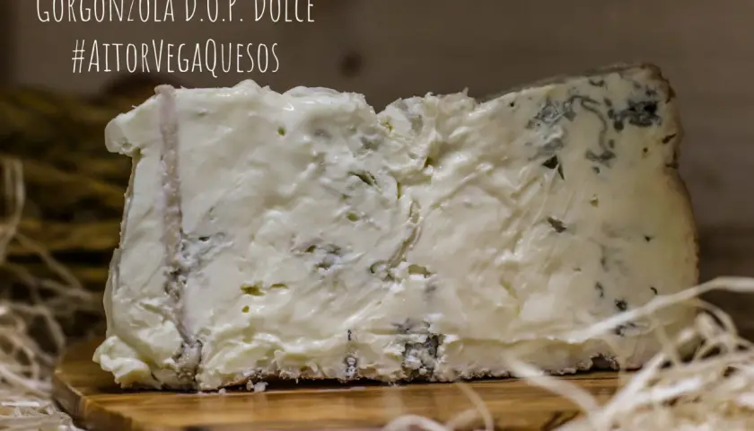 Un trozo de gorgonzola D.O.P. Dolce, un queso azul cremoso con vetas verdes y azules, sobre una tabla de madera.