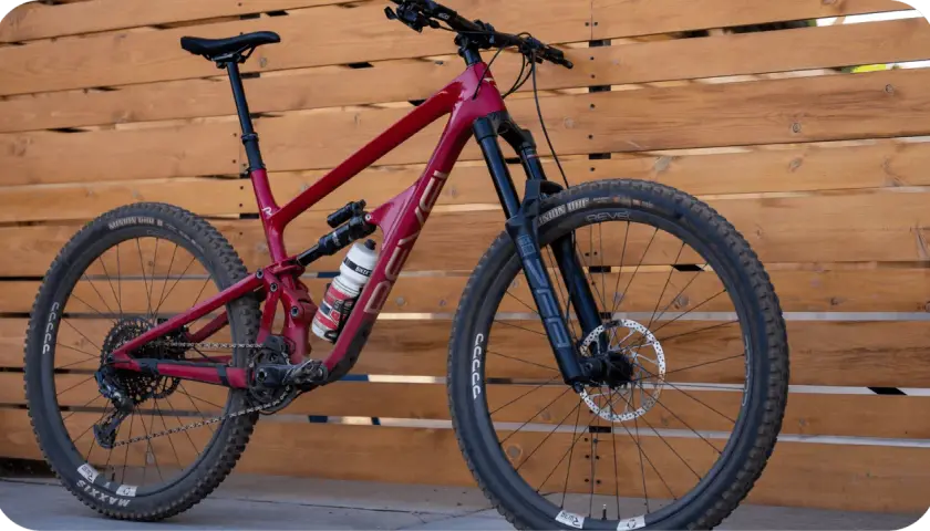 A red Revel Rail mountain bike with a water bottle, parked against a wooden fence.