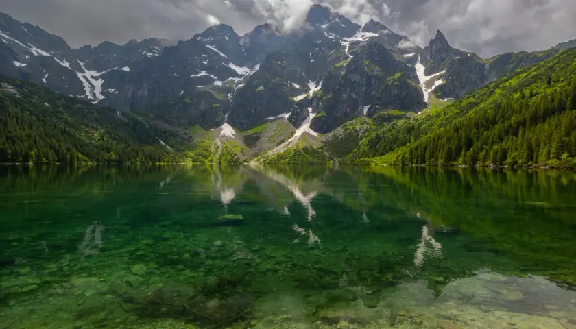 Morskie Oko z rowerem w tle, odbijające się w krystalicznie czystej wodzie. Majestatyczne góry i gęsty las tworzą malowniczy krajobraz.
