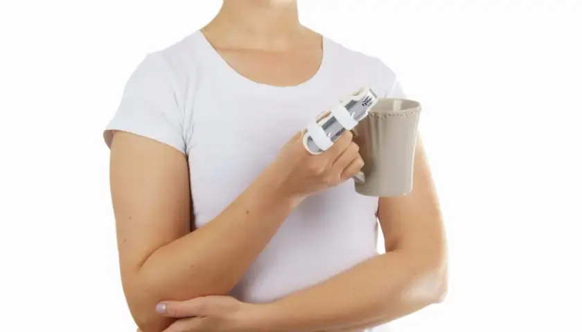 Kobieta w białej koszulce trzyma kubek, a jej palec jest usztywniony stabilizatorem.