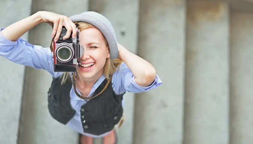 Uśmiechnięta dziewczyna w kapeluszu robi zdjęcie starym aparatem. To świetny pomysł na szkolenie z fotografii!