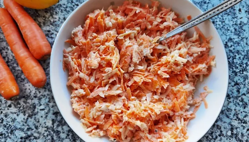 Pyszna surówka z marchewki jak z restauracji, gotowa do podania. Obok leżą świeże marchewki i cytryna.