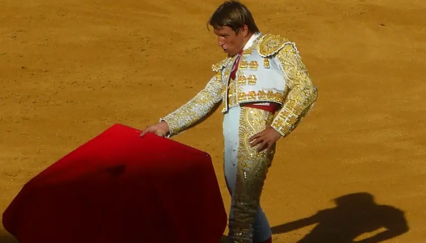 Torero con traje de luces, listo para la faena de muleta, con la capa roja extendida en la arena.