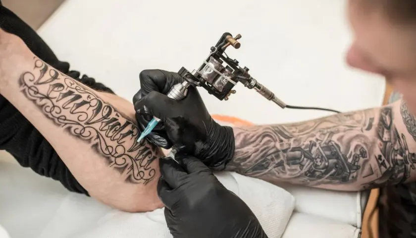 Artysta tworzy nowy tatuaż na przedramieniu klienta, używając maszynki do tatuowania.