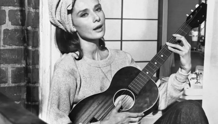 Audrey Hepburn, z ręcznikiem na głowie, gra na gitarze, śpiewając "Moon River".