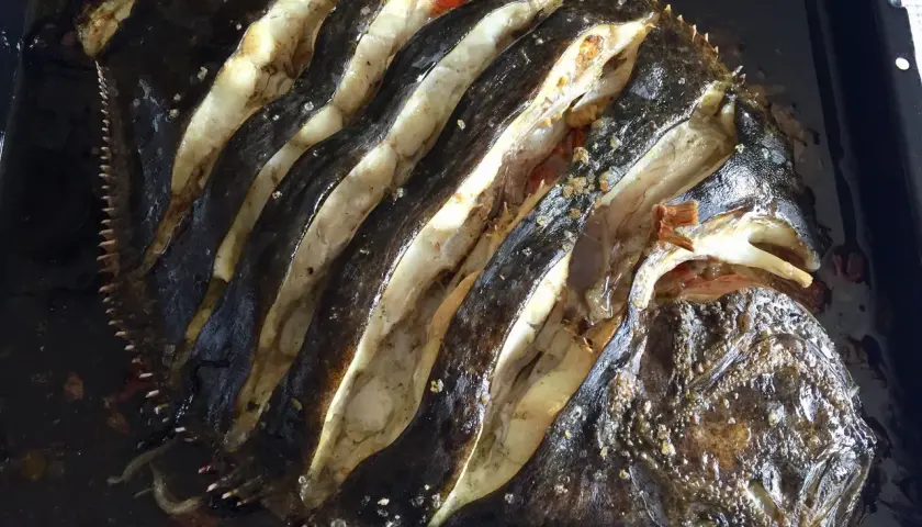 Rodaballo al horno, con cortes profundos que revelan su carne blanca y jugosa, listo para ser disfrutado.