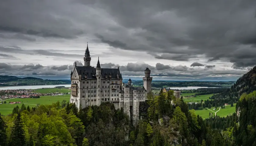 Bajkowy zamek Disneya w Niemczech, Neuschwanstein, wznosi się na skalistym wzgórzu, otoczony zielonymi lasami i malowniczym jeziorem.