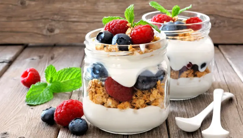 Dos frascos de vidrio con yogur, granola, frambuesas y arándanos. ¡Cuidado! El yogur con avena engorda si no se consume con moderación.