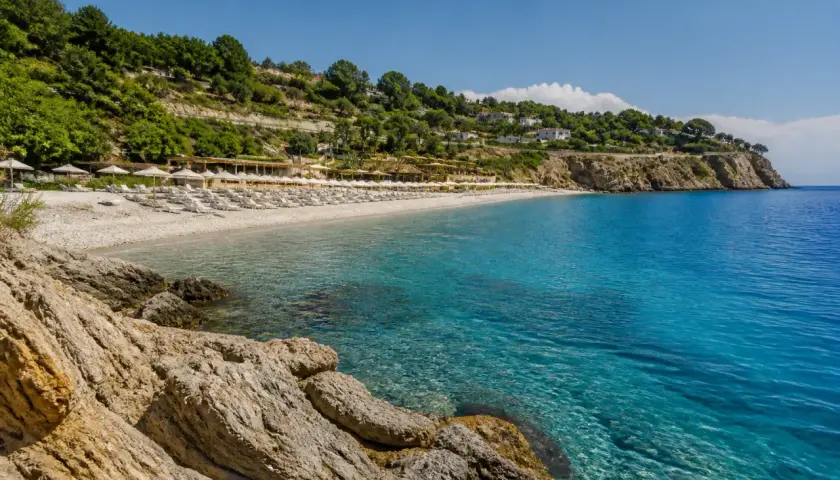 Plage de galets et eaux turquoises à Alassio, Italie. Des rangées de parasols et de chaises longues invitent à la détente sous le soleil.