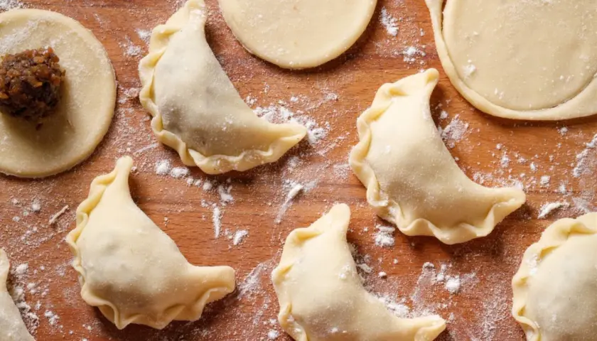 Surowe pierogi z kaszą gryczaną i twarogiem na drewnianej desce, posypane mąką.