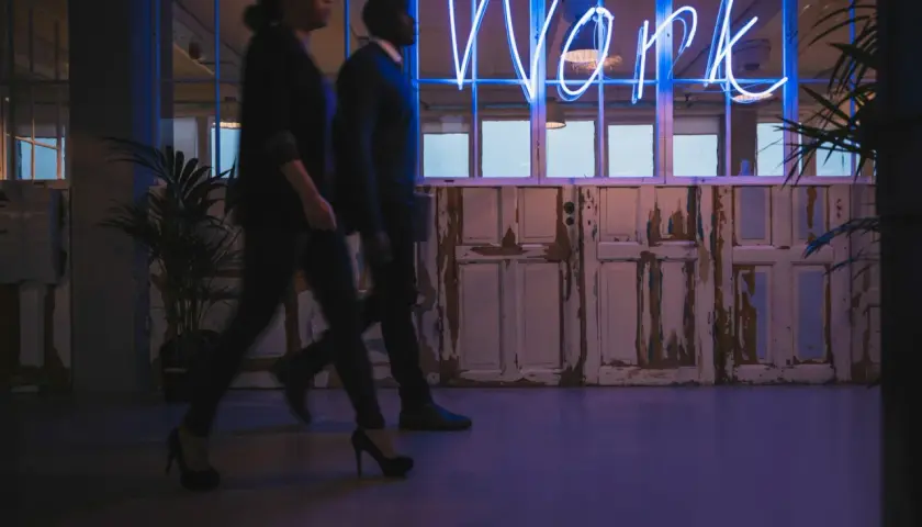 Ludzie idą w stronę neonu "Work", symbolizującego misję i wizję firmy.