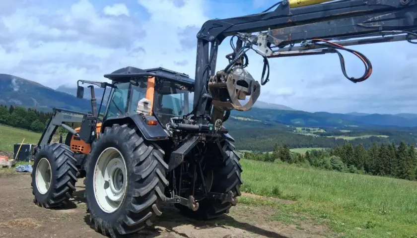 Ein gebrauchter Forstkran mit Greifer an einem Traktor, bereit für den Einsatz im Wald.