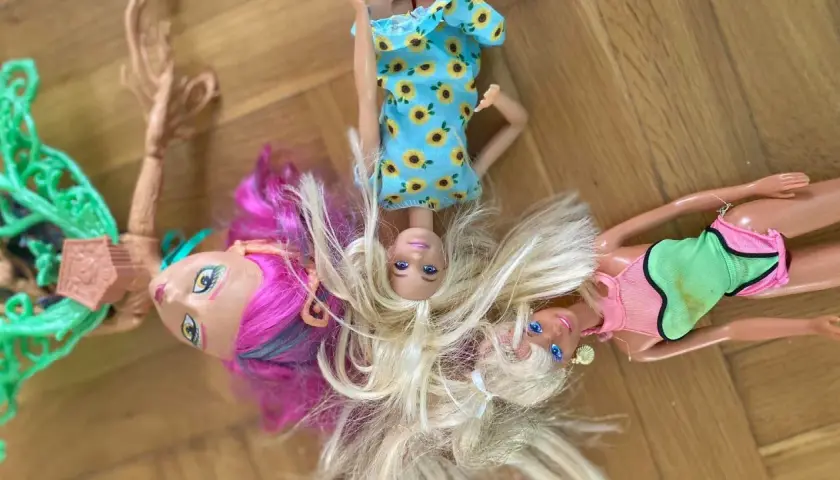 Trzy lalki leżą na podłodze. Jedna ma różowe włosy, druga blond, a trzecia sukienkę w słoneczniki. Dowiedz się, jak rozczesać włosy lalce, by wyglądała jak nowa!