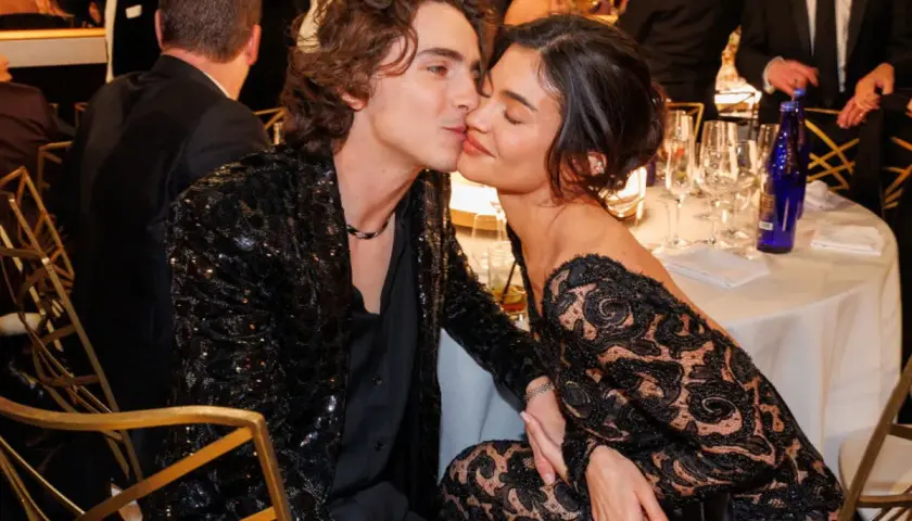 Kylie Jenner i Timothée Chalamet w czarnych, eleganckich strojach, podczas romantycznego momentu przy stole.