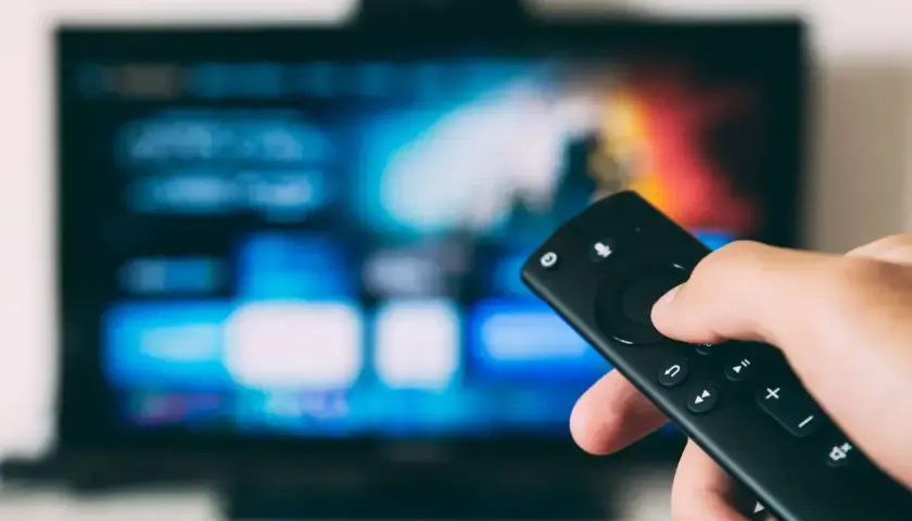 Dłoń trzymająca pilot do telewizora, ekran pokazuje menu. Dowiedz się, jak odbierać TV naziemną bez anteny, korzystając z nowoczesnych rozwiązań.