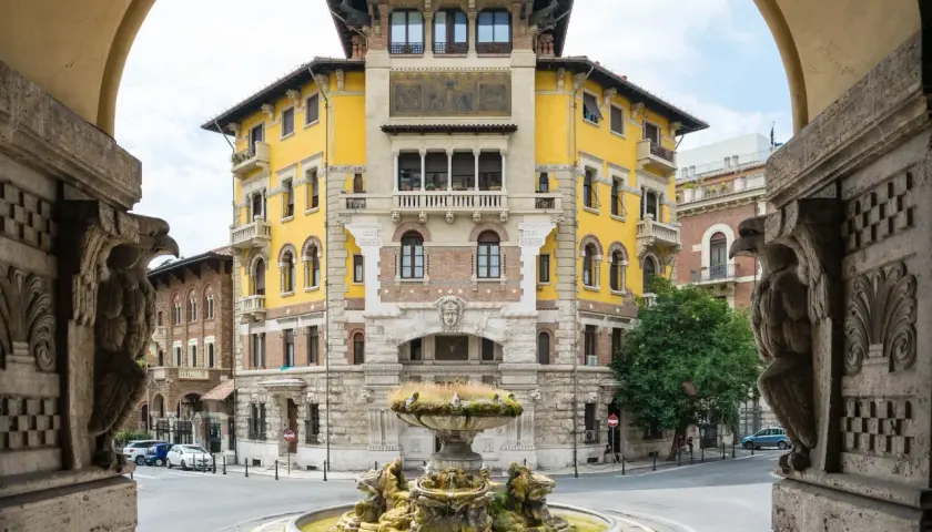 Fontana e palazzo giallo in stile Coppedè, con dettagli scultorei e un'atmosfera d'altri tempi.