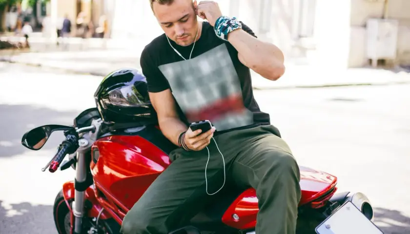 Joven en moto roja ajusta sus auriculares. Disfruta de su música, demostrando que es legal escuchar música en moto.